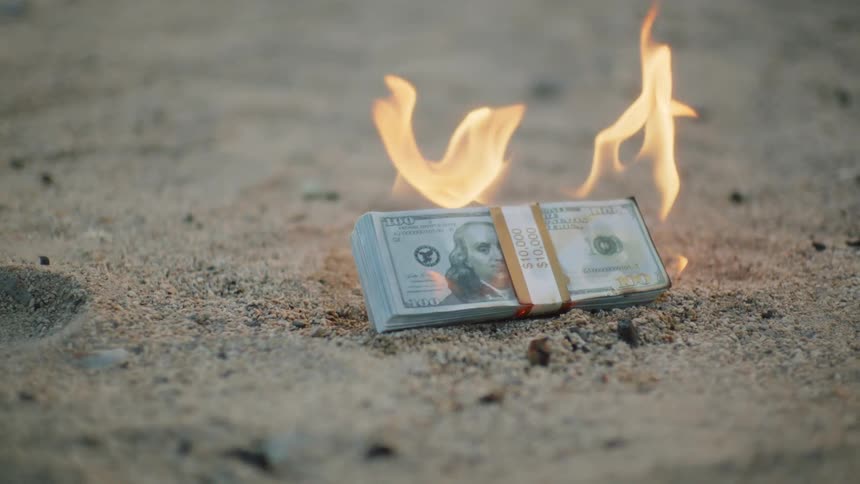 Bundle of dollar bills burning with yellow flames on the sand