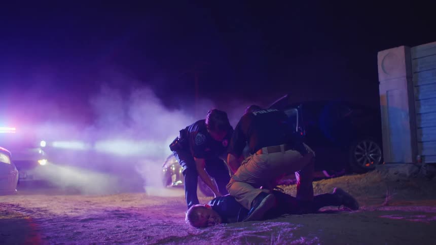 A man lies down in the dirt as police handcuff him