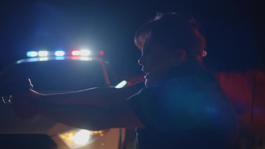 A female police officer holding hear gun outward walks forward while angrily shouting commands