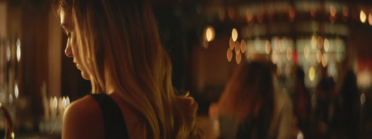A blonde woman waits alone at a crowded bar