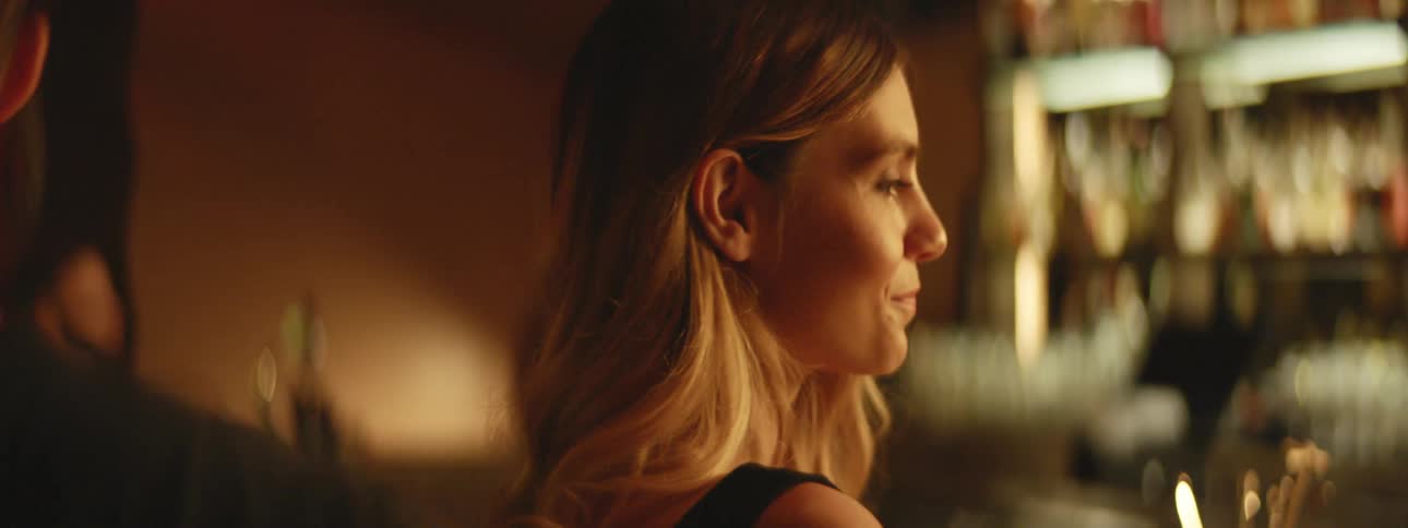 A woman is sitting at the bar looking around at people