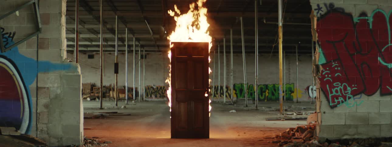 A free standing door stands upright while engulfed in flames within an abandoned building