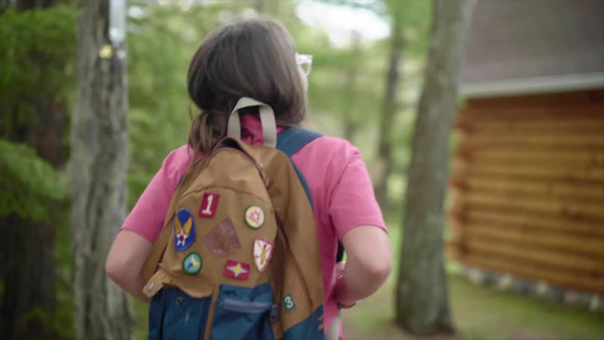 Girl with a backpack and a pink t shirt walks on a forest track next to a house in the countryside