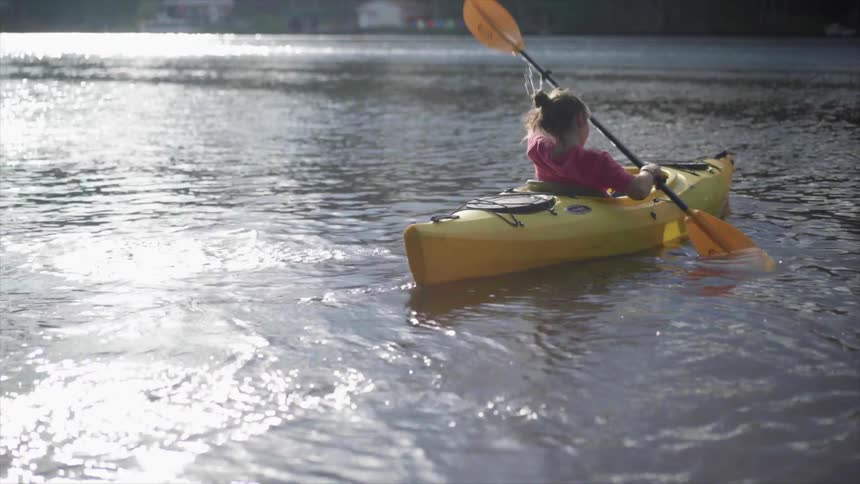 A young woman paddles a kayak away from the shore towards the center of a lake