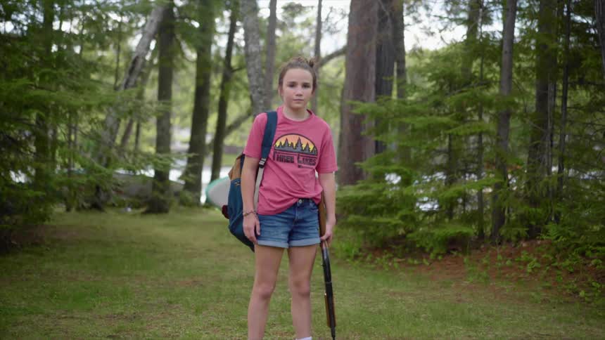 Girl with a backpack and a pink shirt stands and holds a shotgun in the forest
