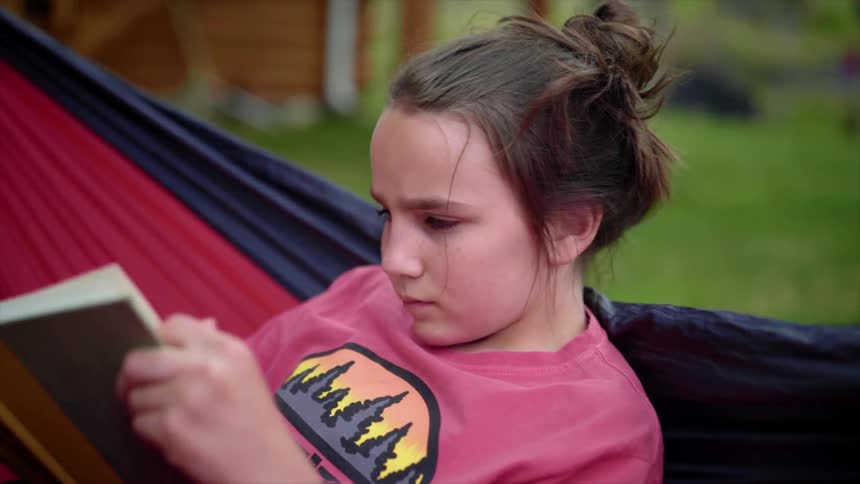 A girl in a hammock outside reading a book