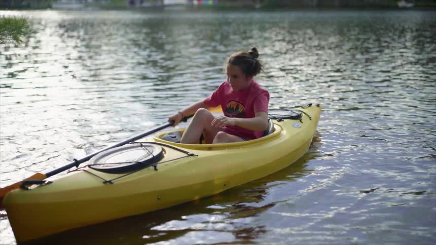 Young female climbs into the seat of kayak and picks up the double sided oar to push the vessel away from the shore line