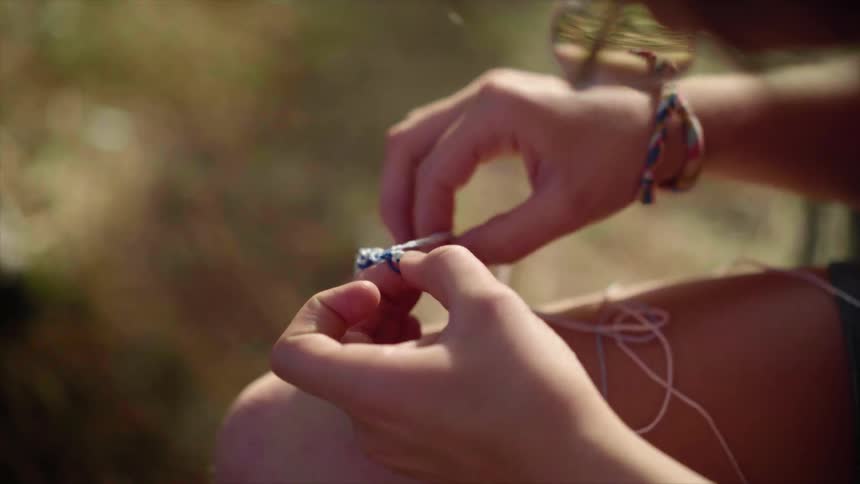 Female straightens out some string while sitting outdoors