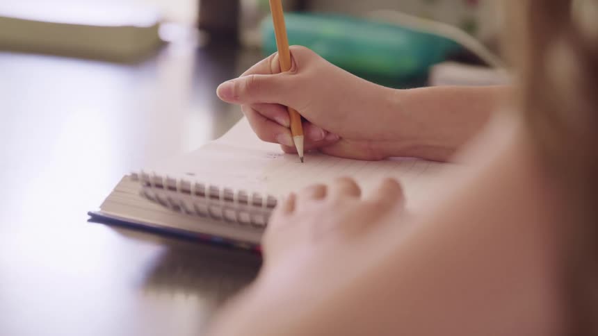 Young girl writes in a book with a pencil
