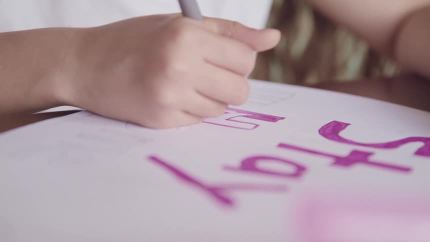 Children writing a stay home sign with purple marker on a table