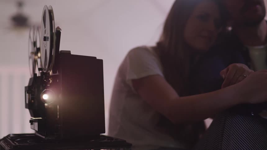 A husband and wife cuddle as they watch film on a projector