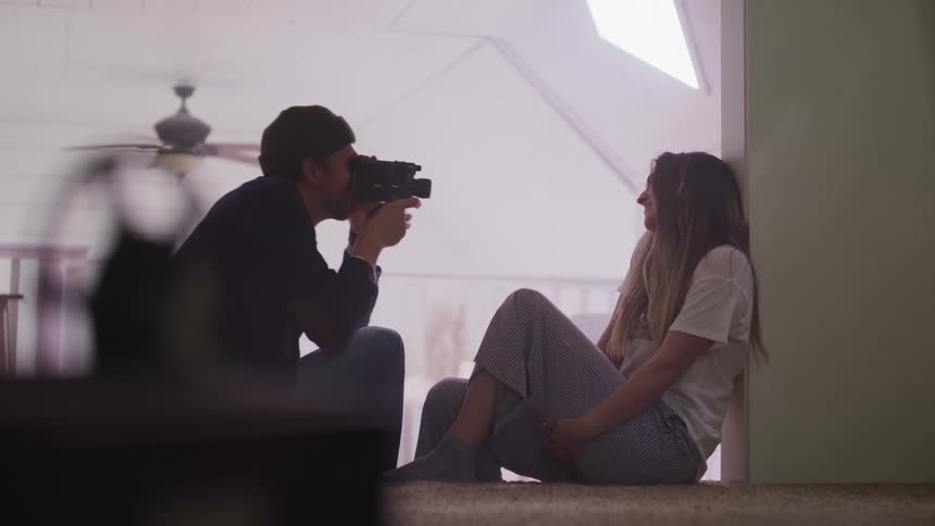 A man is filming a girl sitting on the floor
