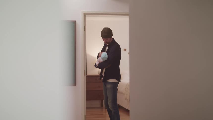 A father holds a newborn while standing in a hallway