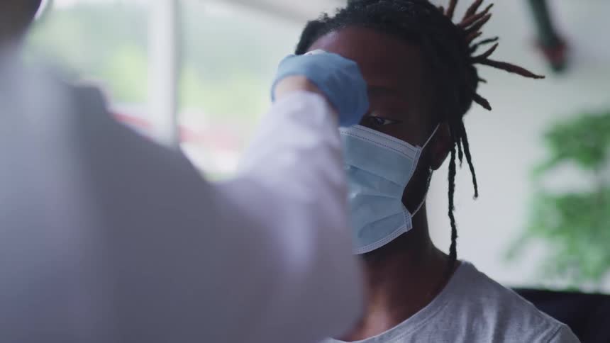 Doctor takes temperature of patient wearing face mask with digital thermometer