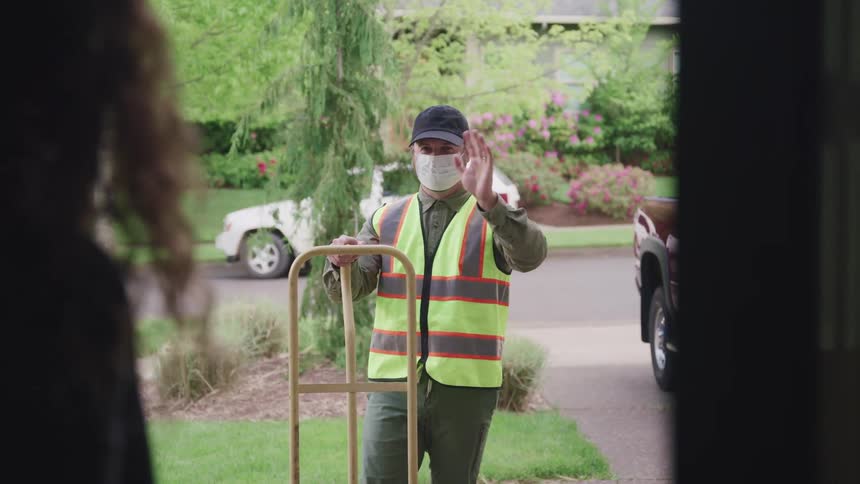 A woman returns the wave of a delivery man outside of her house before he turns away