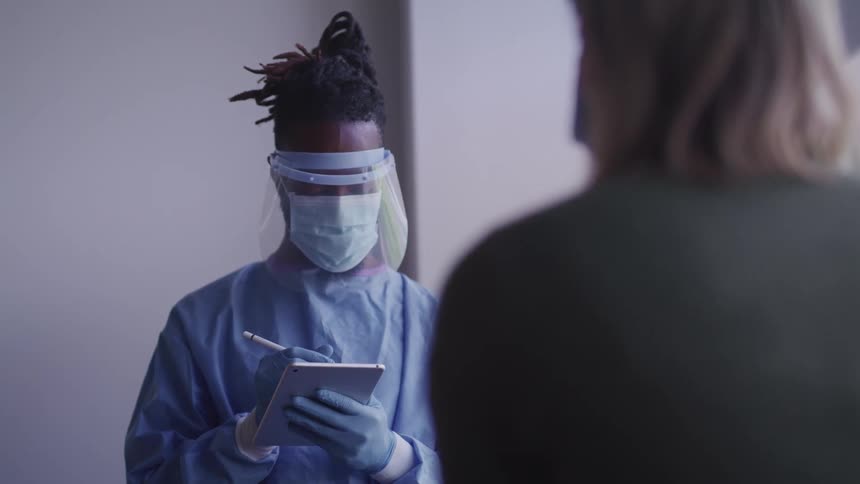 Nurse wearing a mask uses a tablet as she speaks with a patient