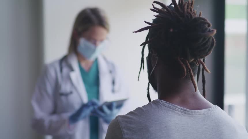 A nurse uses a tablet as a patient sits in a clinic