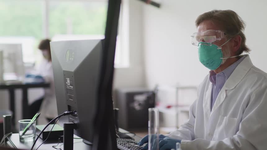 A doctor with a mask goggles and gloves typing on a computer