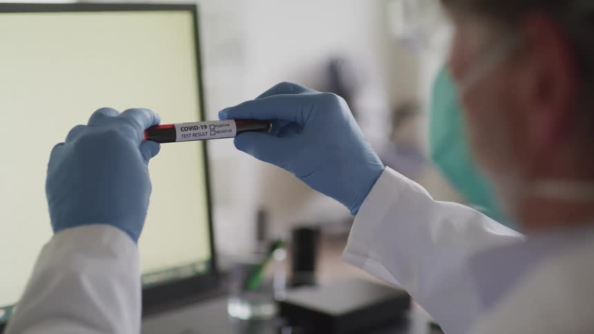 A laboratory working in a white lab coat holds a sealed test tube while looking at its label