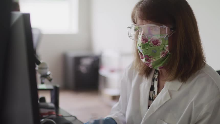 Doctor wearing goggles and a mask works on a computer in an office