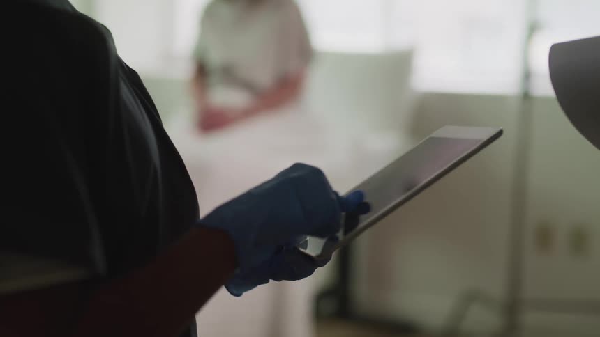 A patient sits on an exam table and a nurse scrolls through a tablet