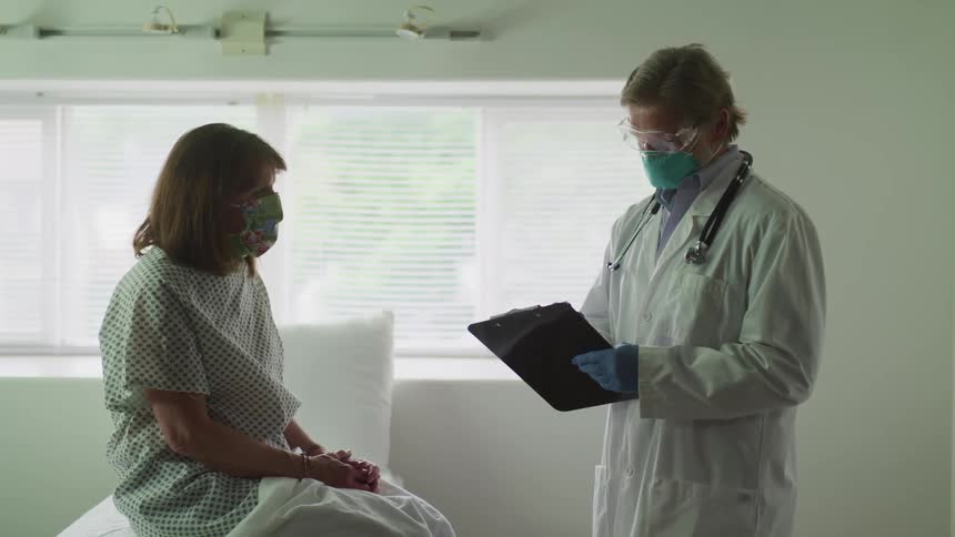 A doctor and patient both wear masks while talking in a clinic room