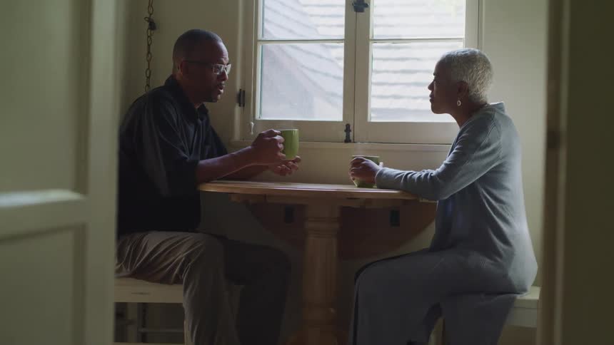 A man and woman sitting at a table talking drinking tea