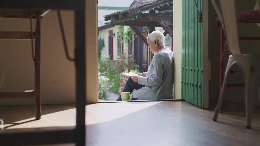 Female sitting on porch reading a book with the front door open and a coffee mug beside her