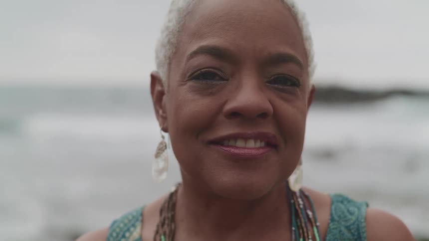 A woman is smiling outdoors by the ocean