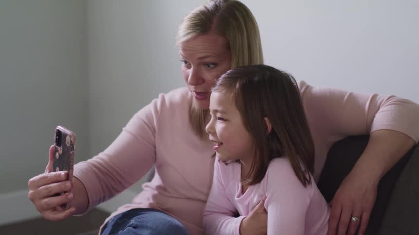 A mother and her daughter talk and wave to someone on a cell phone