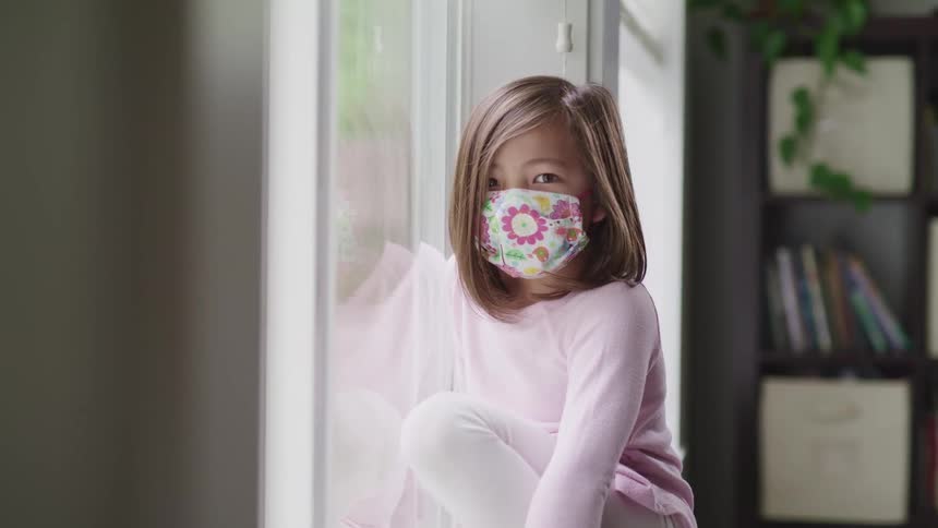 A child with a mask sits looking out the window