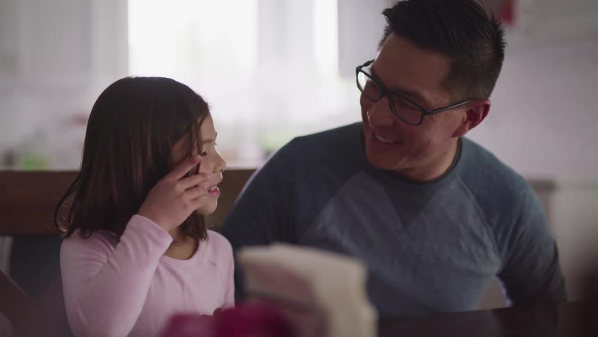 A man smiles at a little girl sitting beside him at a table