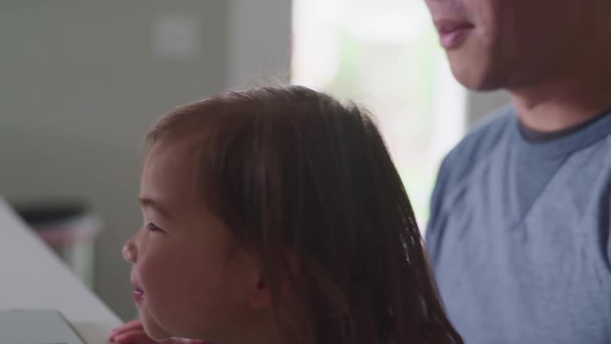 A man shows points something on the screen of his laptop out to a smiling little girl