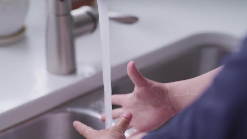 A little boy puts his hands under a faucet with running water