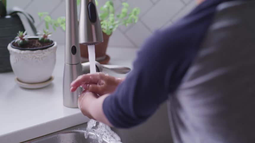 Washing hands under a faucet at kitchen sink