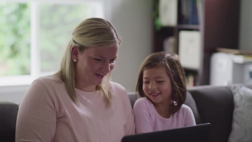 Woman and girl sit on couch viewing computer screen