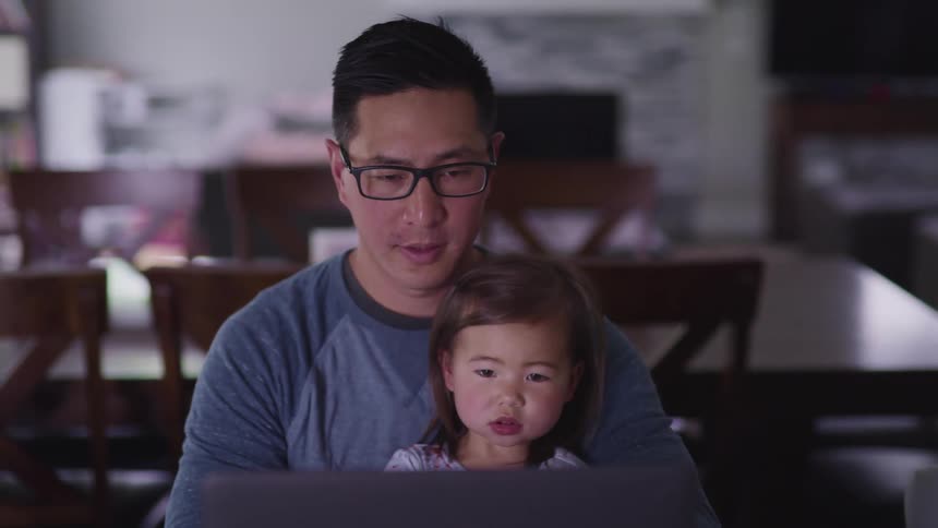 Father with daughter on his lap sit in front of a laptop at home
