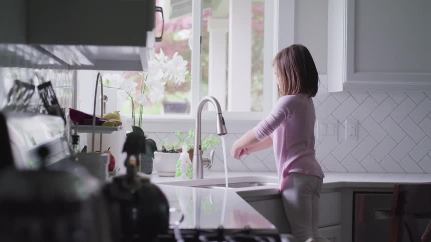 A young girl washes her hands at a kitchen sink