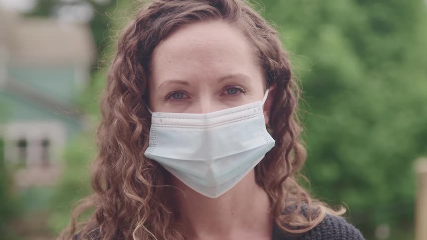 A woman is standing outdoors while wearing a face mask