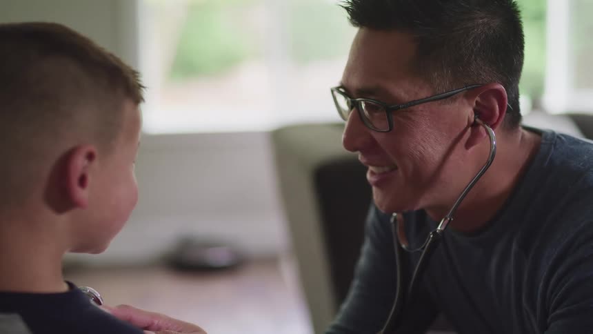 A man with a stethoscope and glasses listening to a boys heart