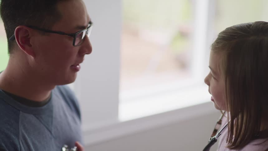Daughter holds the end of the stethoscope up against her fathers chest to listen to his heart beat while looking at him with amazement