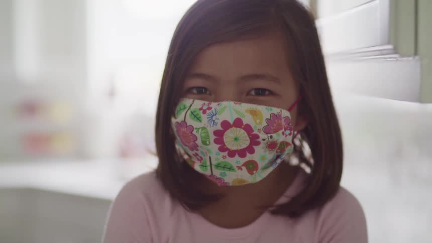 A young girl wears a floral face mask indoors
