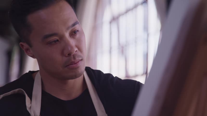 An artist paints on a canvas indoors