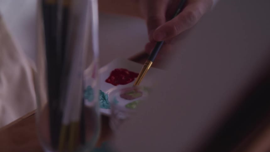 A painter mixes colors on a small plate on a table with an easel