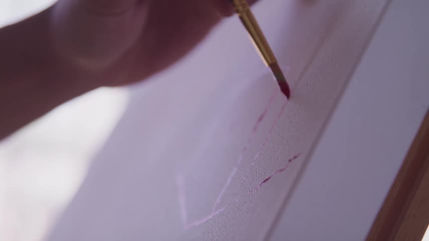 A persons hand holding a paint brush painting on a canvas