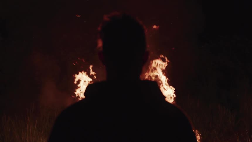A man is walking outdoors next to a fire