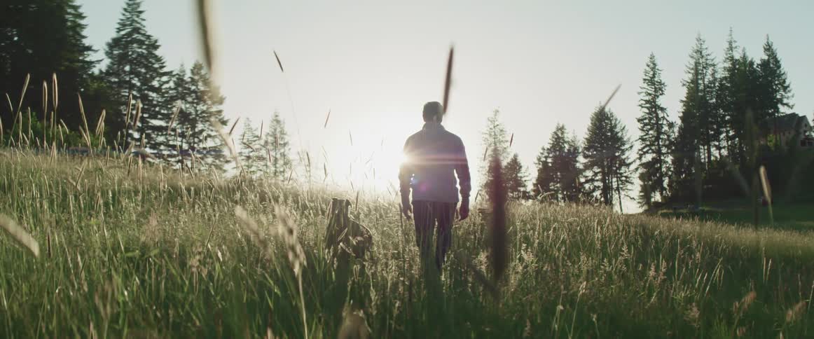 A man walks across a grass field with his dog