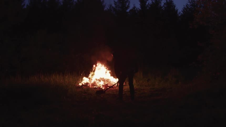 A man shovels dirt in front of a bonfire
