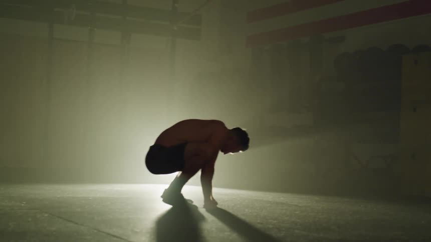Man in shorts crouches down then lays back on the floor while a bright light shines on him
