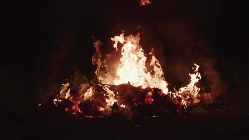 Firewood burns and flames grow higher at a bonfire at night
